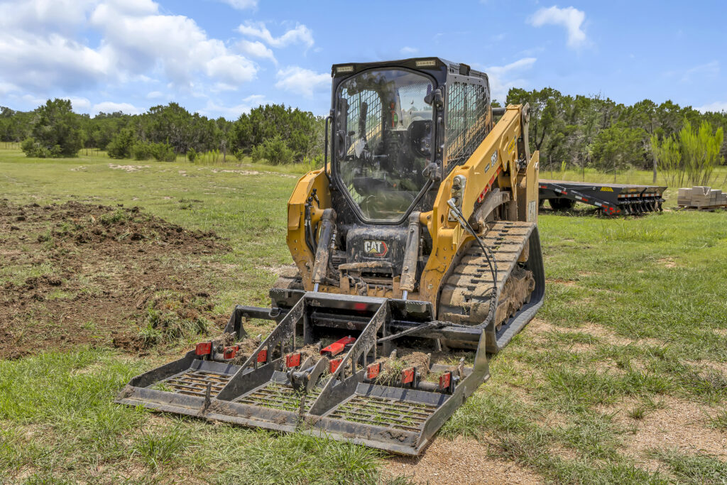 Track loader with a driveway leveling attachment working pasture land in Bertram, TX