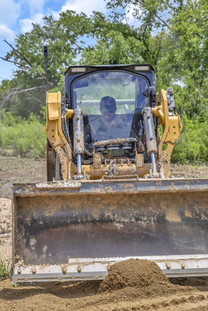 Skid steer operator grading soil with a dozer blade during land clearing work on a job site