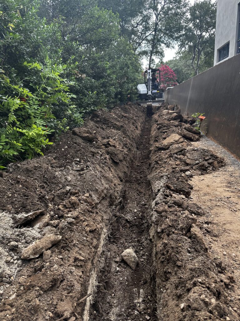 Trench excavation for utility and drainage installation alongside a residential property